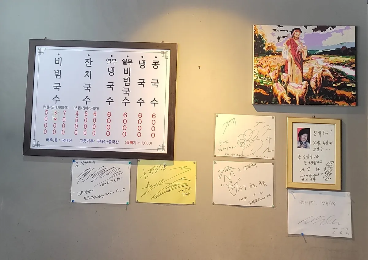 강화국수 가게 벽. 메뉴판 옆에 사인 액자 여섯 장이 붙어 있다.