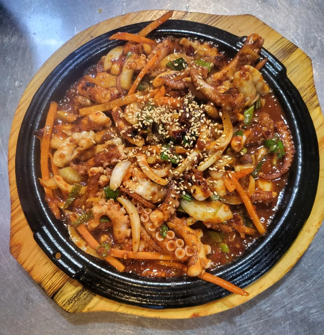 모래성분식포차 직화낙지볶음. 검은 무쇠 팬에 낙지, 양파, 채 썬 당근, 쪽파, 깨가 담겼다. 값은 23,000원이다.