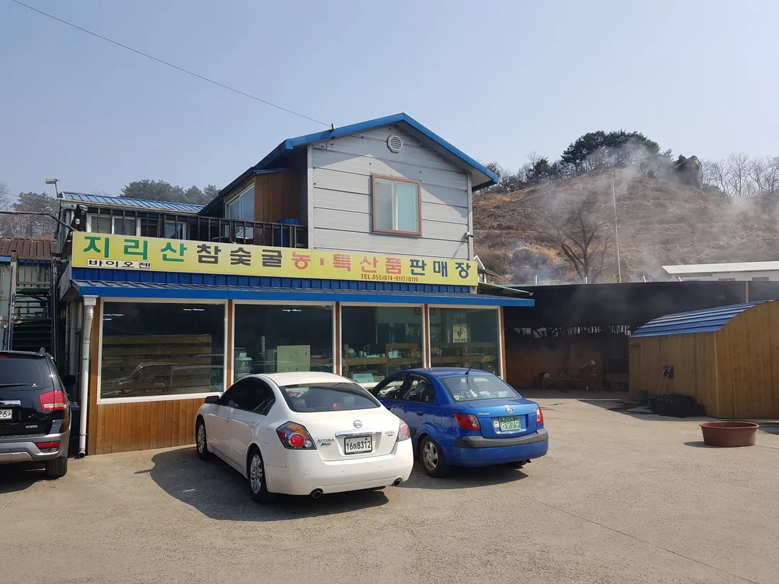 「지리산참숯굴 농·특산품 판매장」 노란 간판이 걸린 이층 건물과 주차장. 간판에는 전화 055-974-0117과 0119가 나란히 적혀 있다.