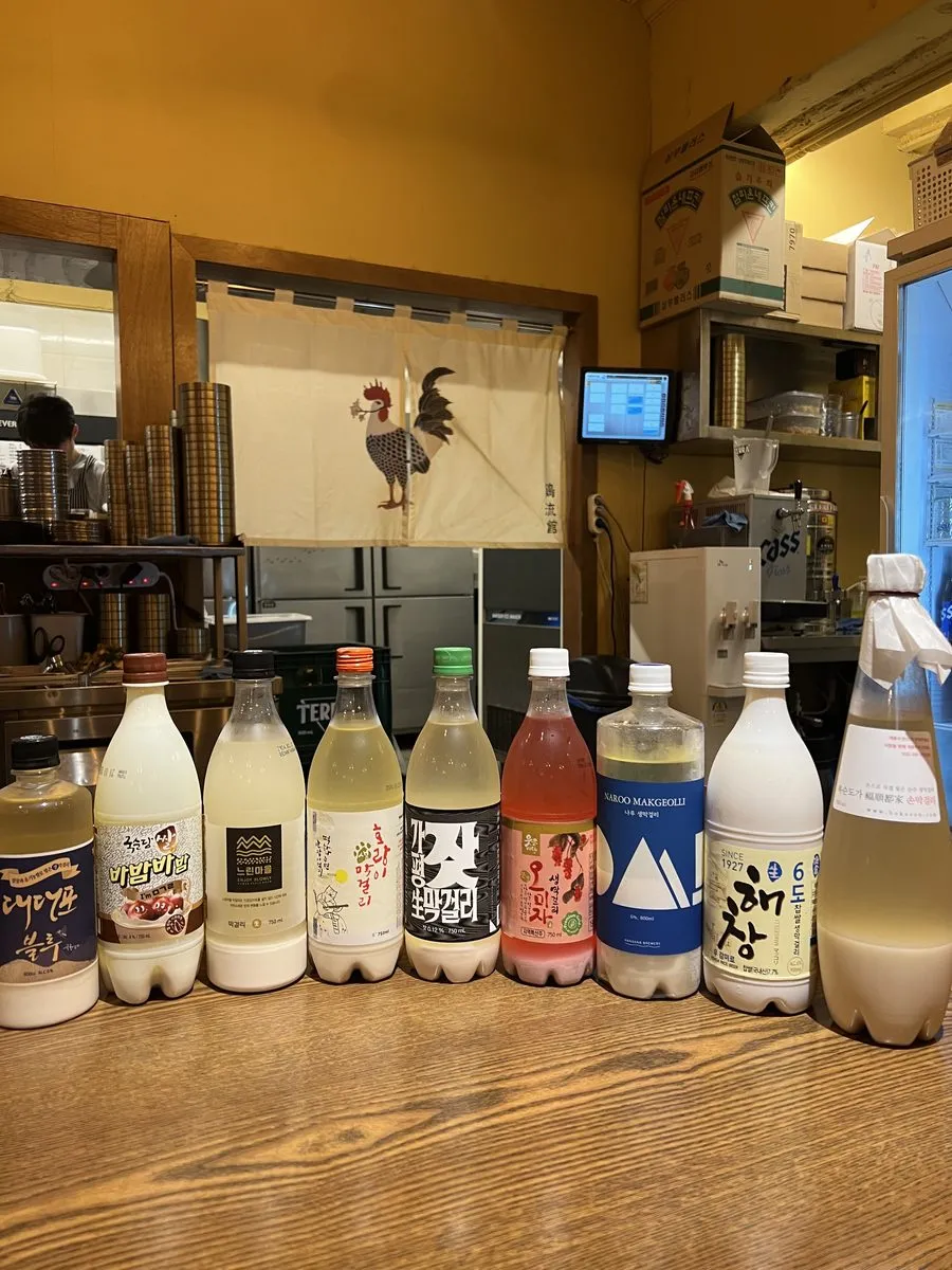 신당 계류관 바 위에 놓인 막걸리 병 아홉 개. 대대포 블루와 밤이면 밤마다, 느린마을, 호랑이 막걸리, 나루 막걸리, 해창 6도 라벨이 보인다.