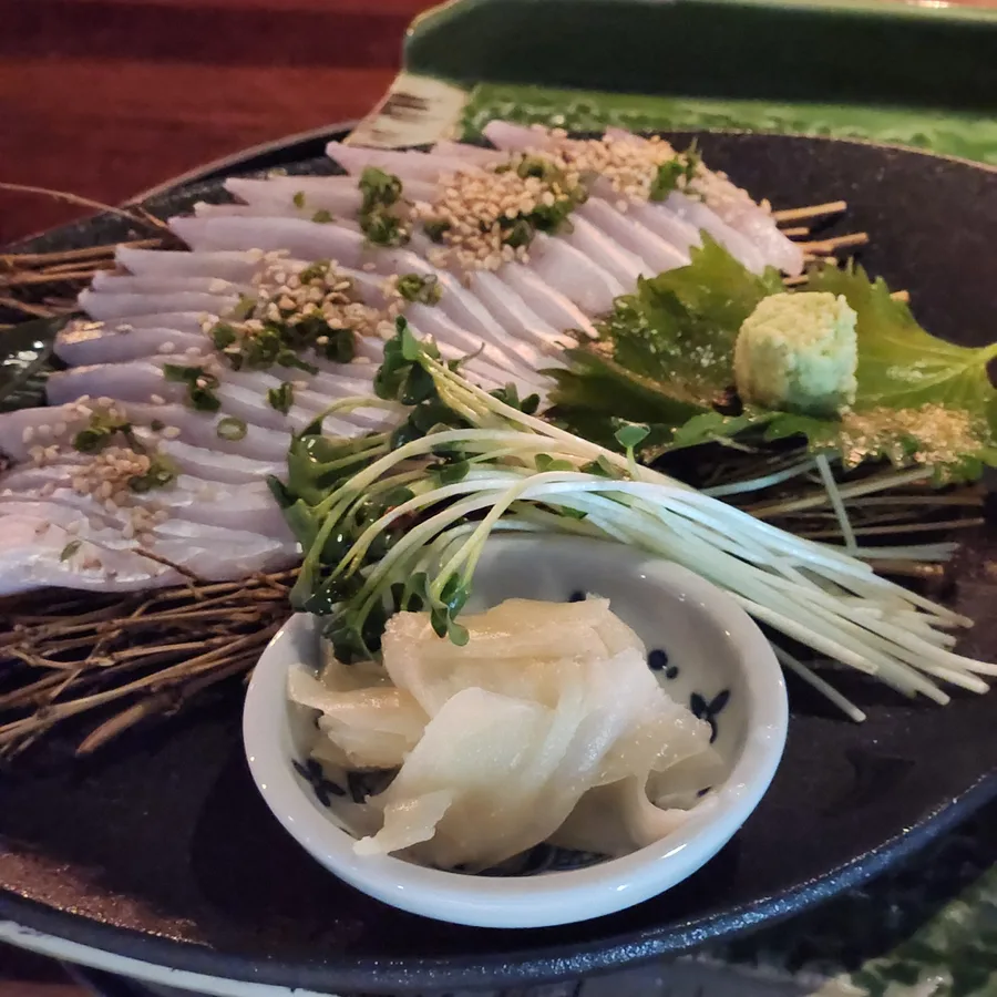 검은 접시에 회를 부채꼴로 깔고 통깨와 다진 쪽파를 뿌렸다. 짚 위에 놓였고 무순과 실파 다발, 초생강 종지, 고추냉이, 깻잎이 곁들여졌다.