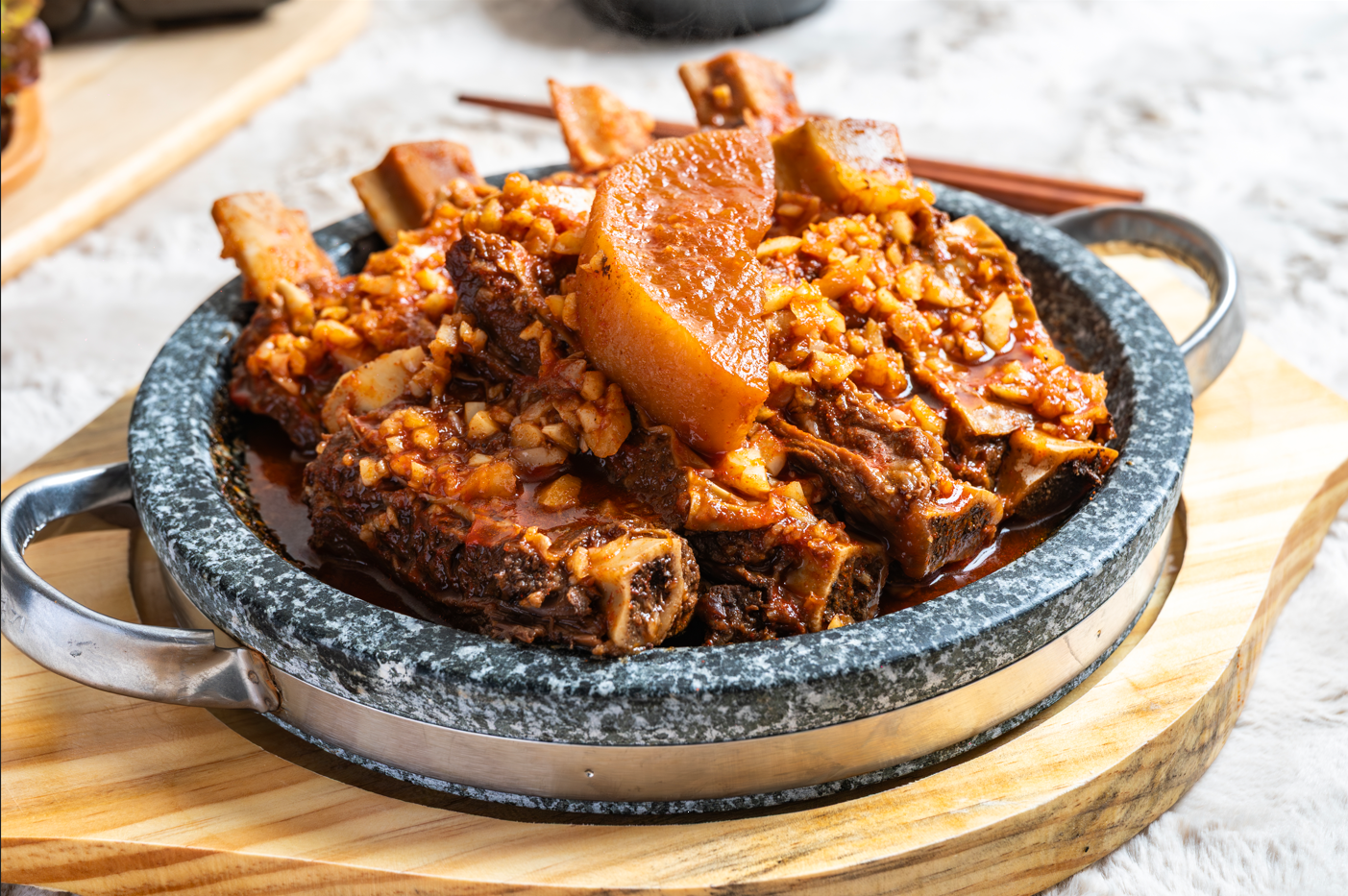 돌판에 담긴 소갈비찜, 갈빗대 네 대와 다진 마늘 양념, 가운데 무 한 점
