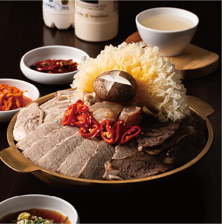 을지하옥 한우 어복쟁반. 놋쟁반 가장자리를 따라 얇게 썬 편육을 둘러 담고 가운데에 표고버섯과 흰 버섯, 붉은 고추를 올렸다. 옆에 육수 그릇과 곁반찬이 놓여 있다.