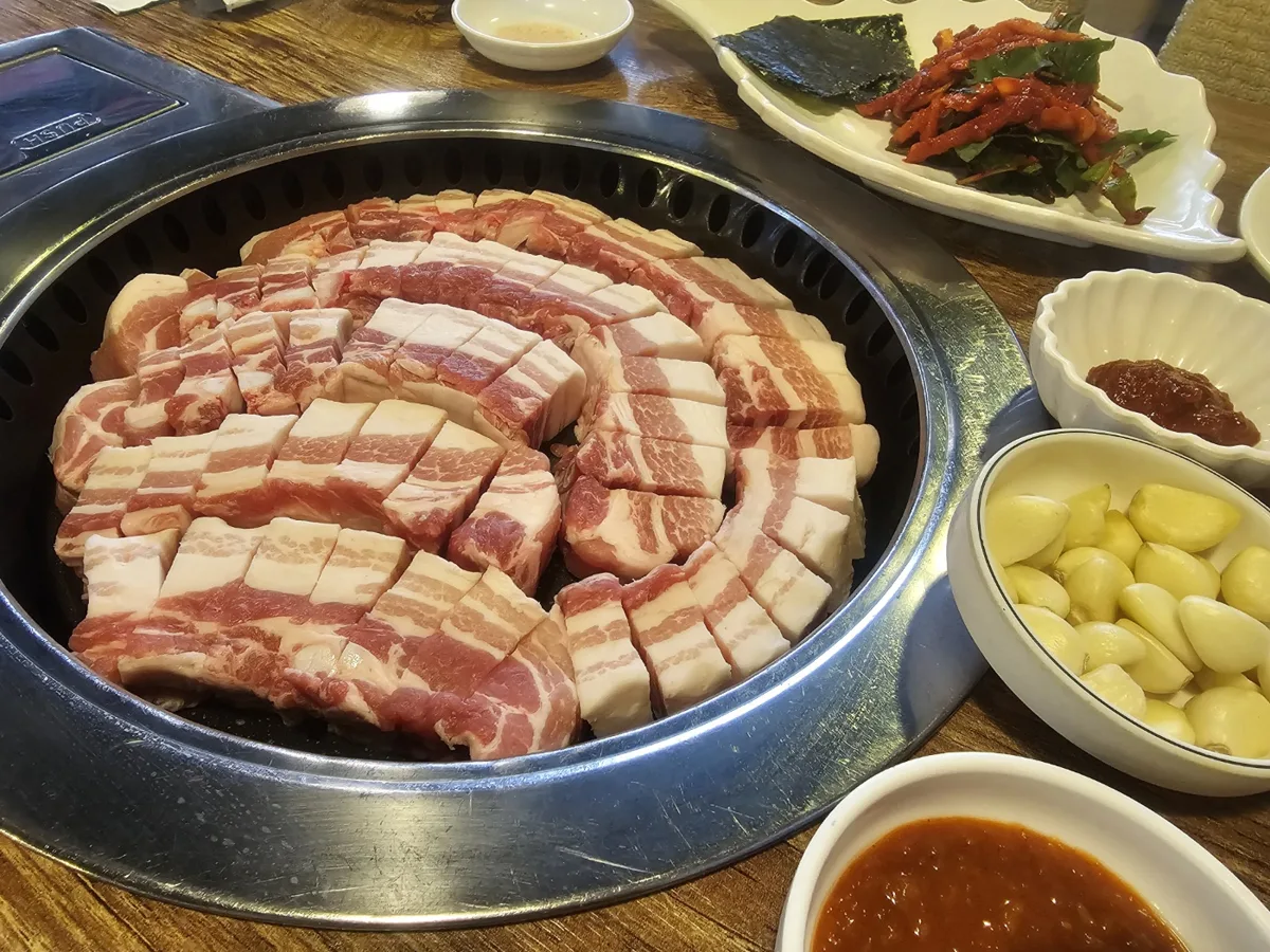 몽화가락이 네이버 플레이스에 올린 삼겹살 사진. 둥근 무쇠 불판 위에 칼집을 넣은 두툼한 삼겹살이 둘러 놓여 있고 옆에 마늘 한 그릇과 쌈장, 고추무침이 놓여 있다.