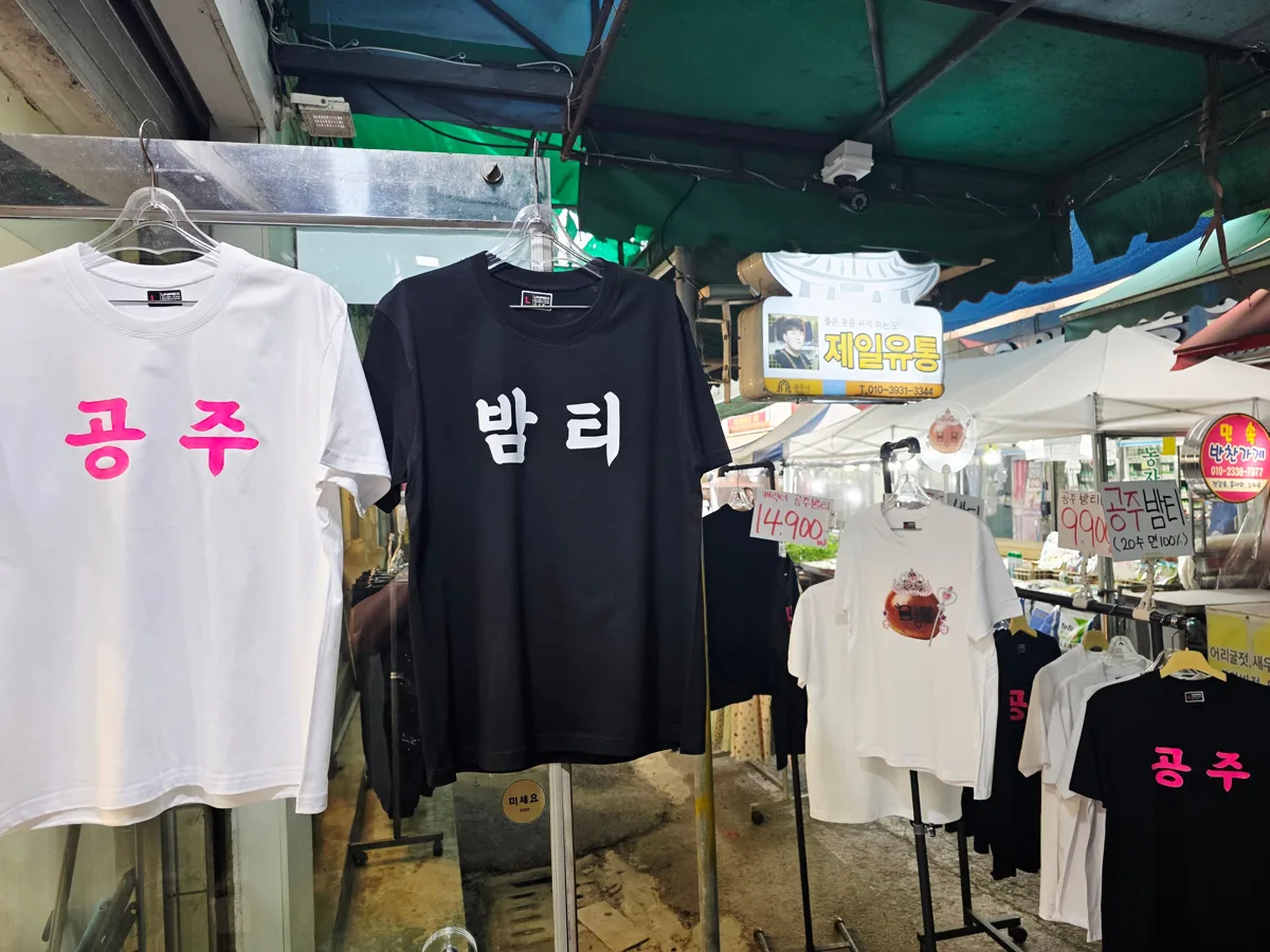 제일유통 좌판에 걸린 공주 흰 티와 밤티 검정 티, 뒤에 가게 간판이 보인다