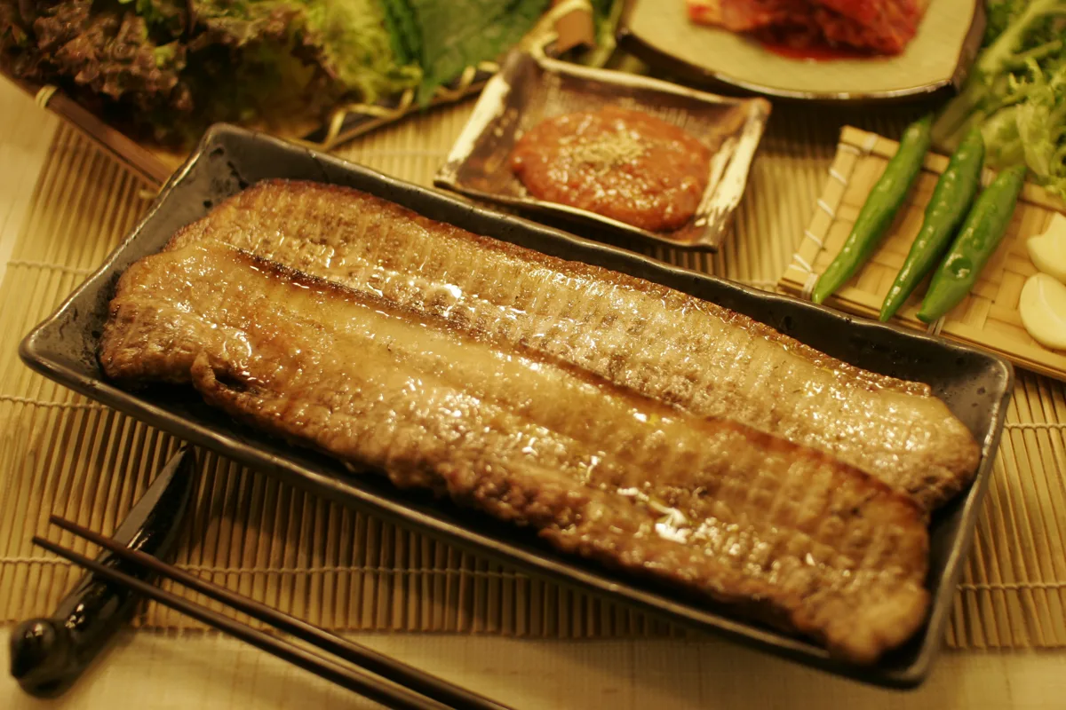 진미실비 검은 접시에 통으로 구운 고기 두 줄, 쌈장과 풋고추, 마늘, 상추, 김치가 함께 놓여 있다